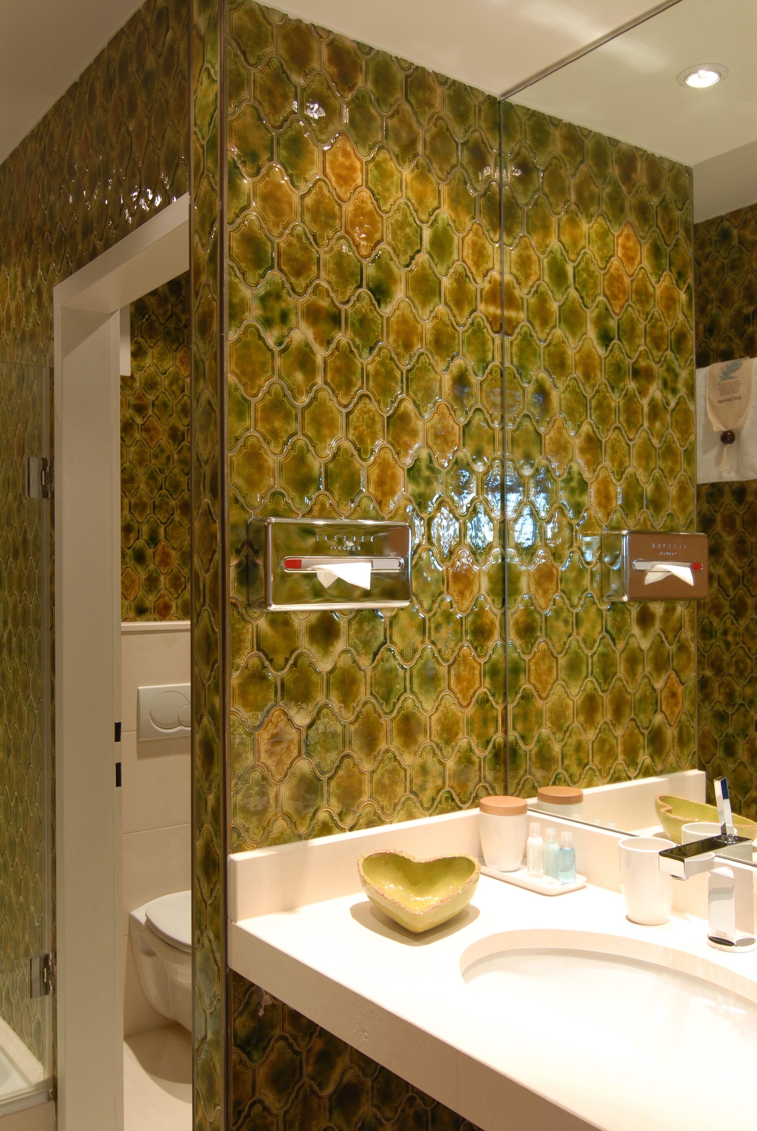 Un baño con pared de azulejos estampados, un lavamanos blanco y un espejo.