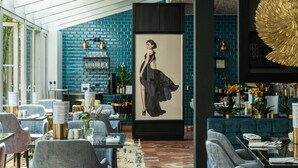Un intérieur moderne avec un mur en briques bleues, une grande œuvre d’art encadrée et différents espaces de détente, comprenant des tables et des chaises.