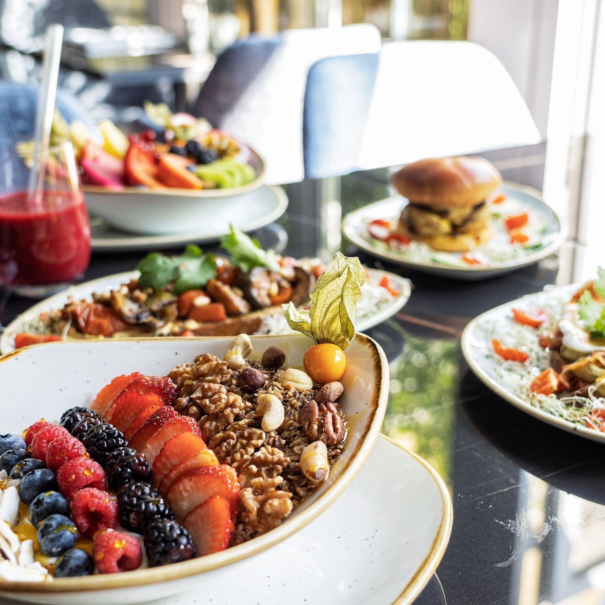 A dining table with various dishes, including a bowl of mixed nuts and berries, a plate with a burger, and a salad.