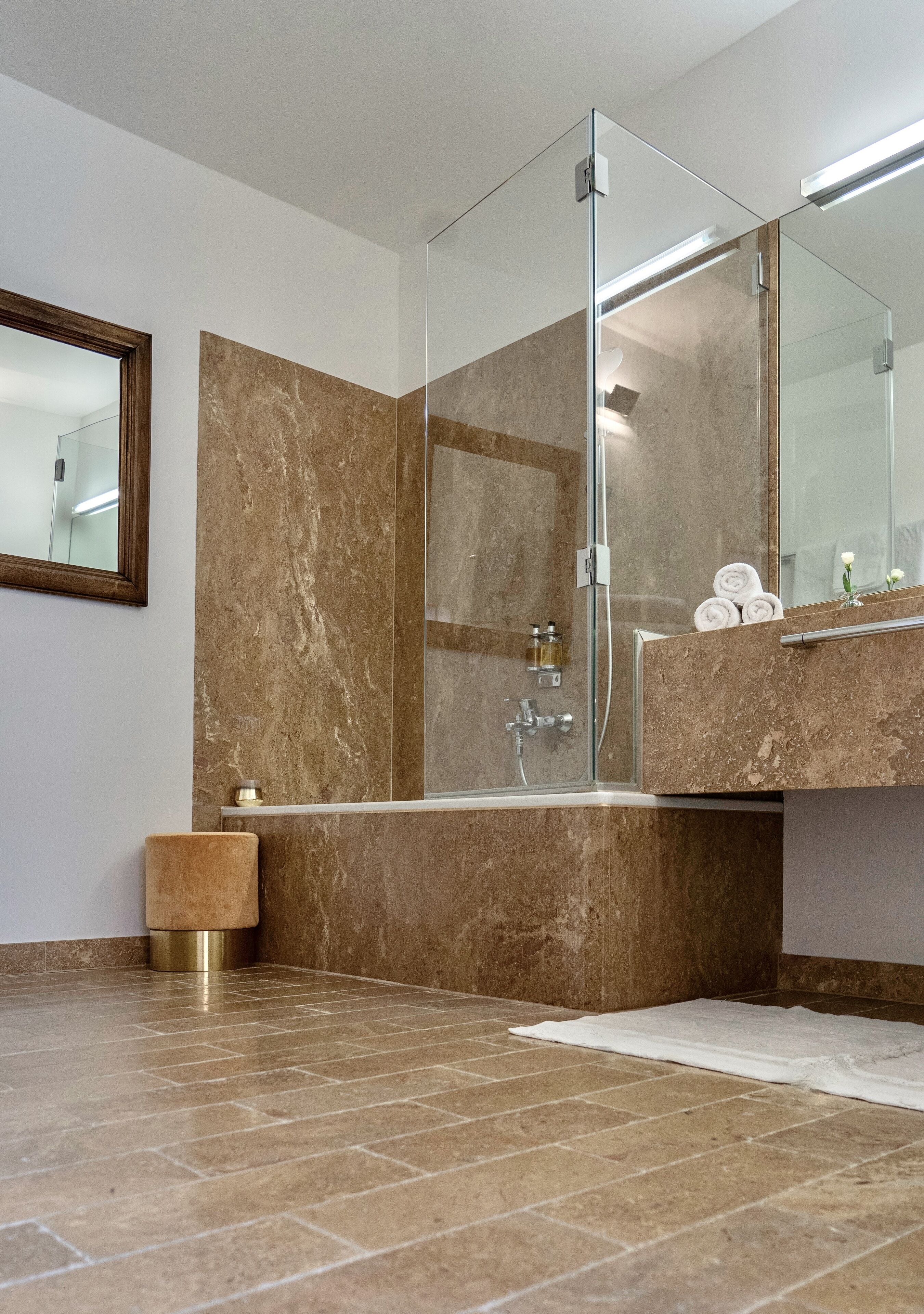 Un baño moderno con cabina de ducha de vidrio, suelo de mármol y un espejo grande sobre el lavamanos.
