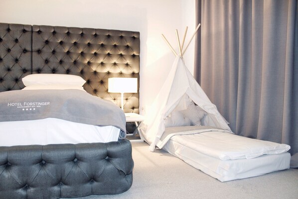 A hotel room with a tufted headboard, a bed with white bedding, a bedside table with a lamp, and a white teepee-style tent. - Hotel Forstinger - Boutiquehotel Schärding (Schärding)