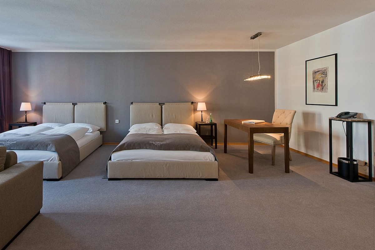 A hotel room with two beds, a sofa, a table, and a chair.