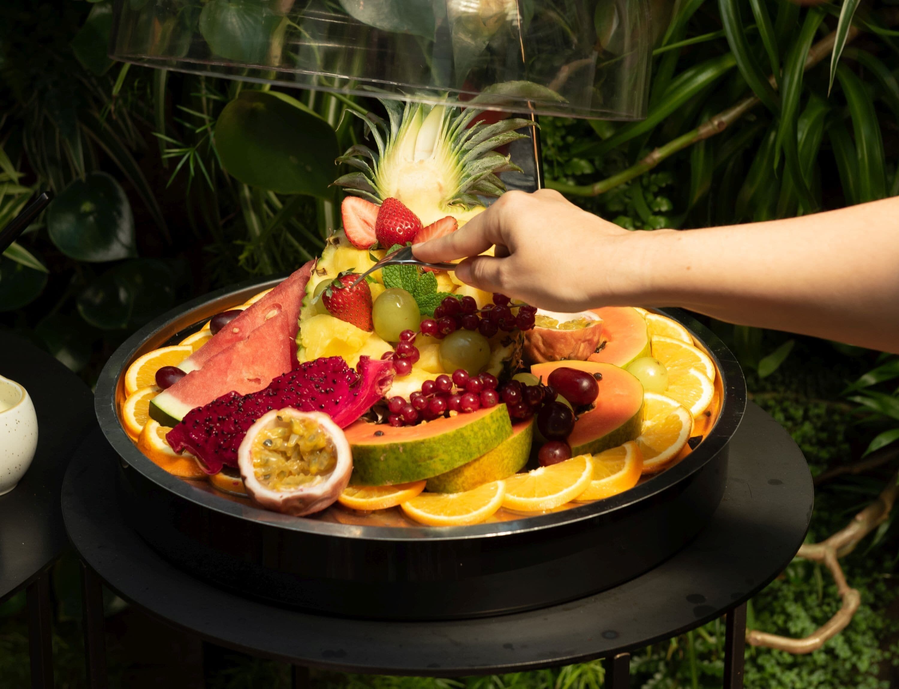 A fruit platter with a variety of fruits including strawberries, grapes, and dragon fruit, arranged on a black tray.