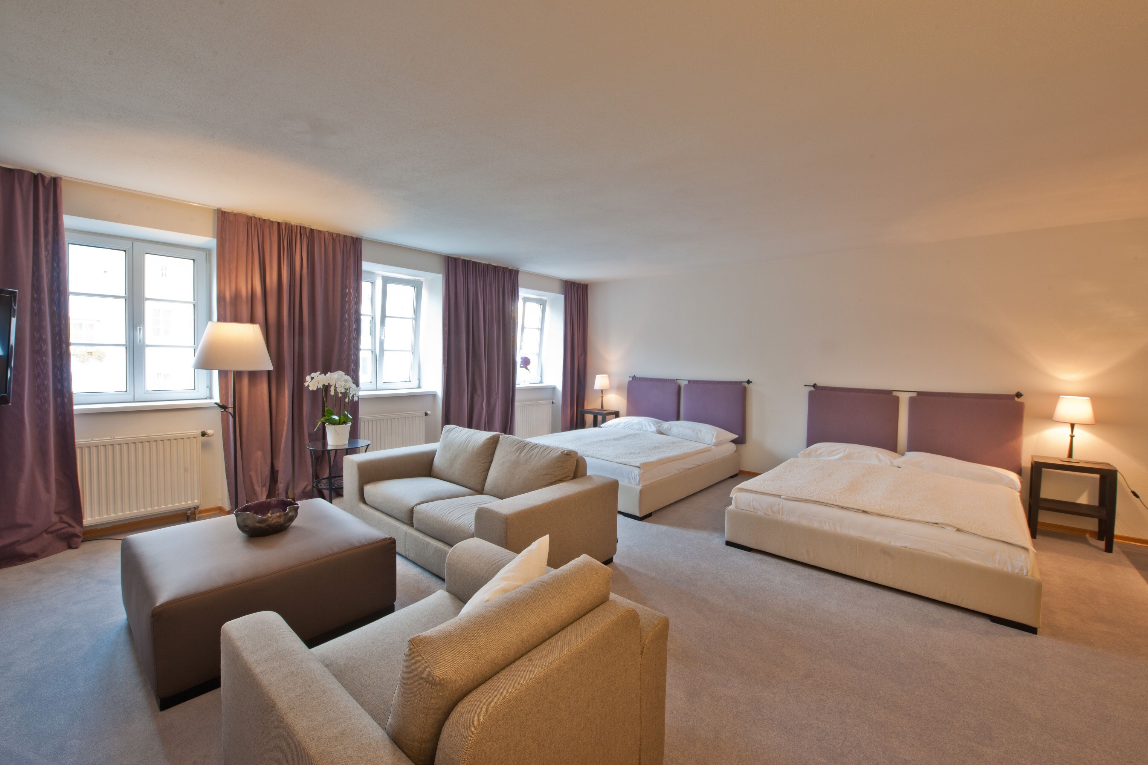 Quarto de hotel com sofá, cama, mesinha com abajur e janela com cortinas.