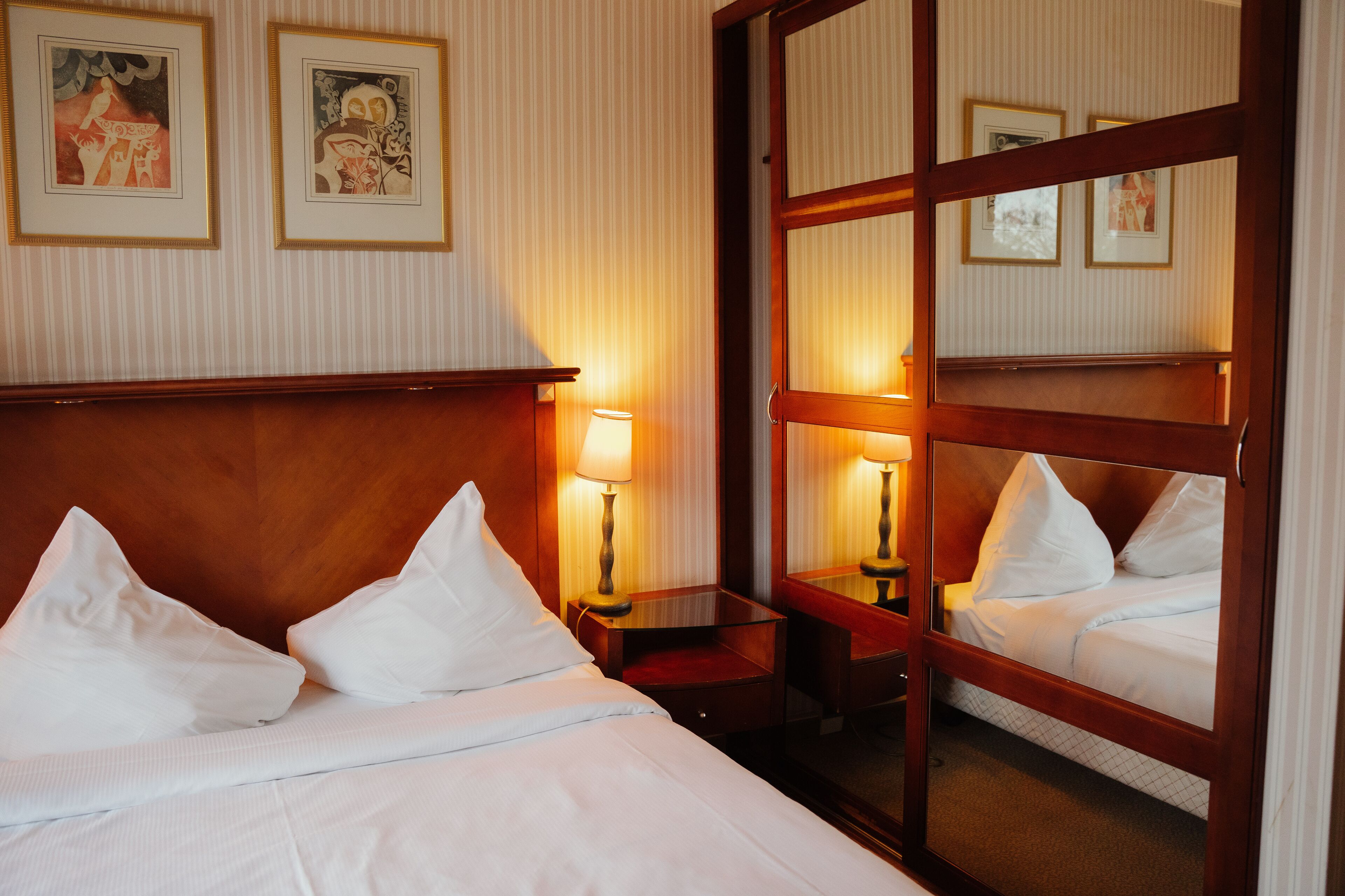 Quarto de hotel com uma cama, duas mesas de cabeceira com luminárias e um espelho grande que reflete a cama e o quarto.
