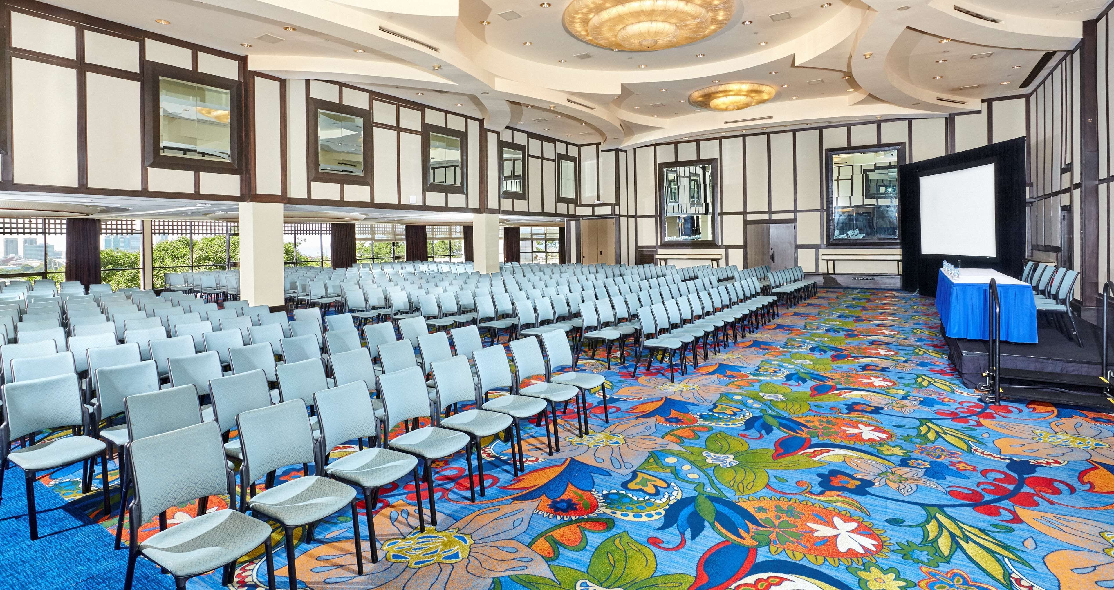 Un salón de conferencias con filas de sillas, un escenario y una alfombra colorida.
