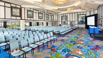 Un salón de conferencias con filas de sillas, un escenario y una alfombra colorida.