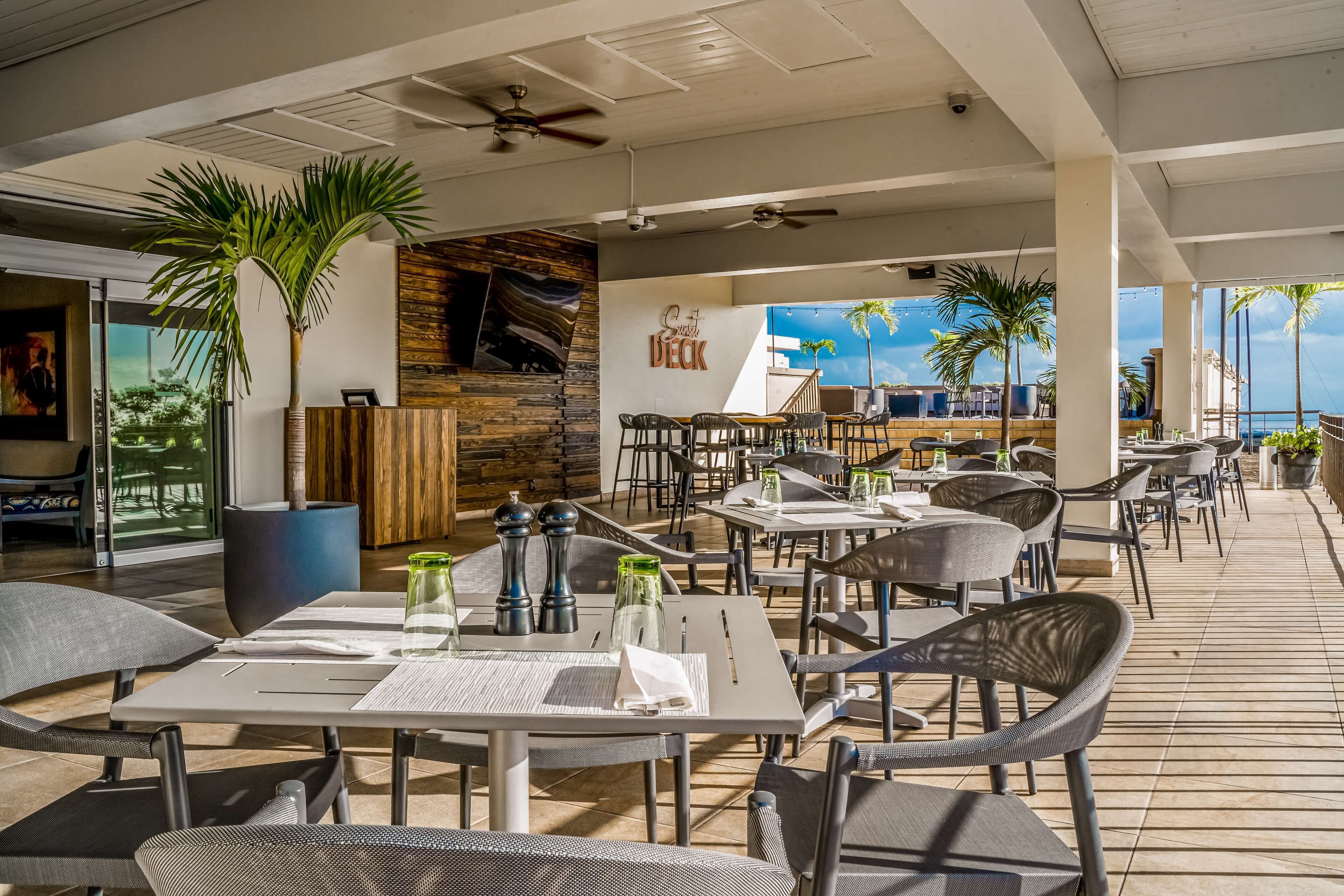 An outdoor dining area with tables and chairs, a wooden wall, and a sign that reads "Sushi Deck".