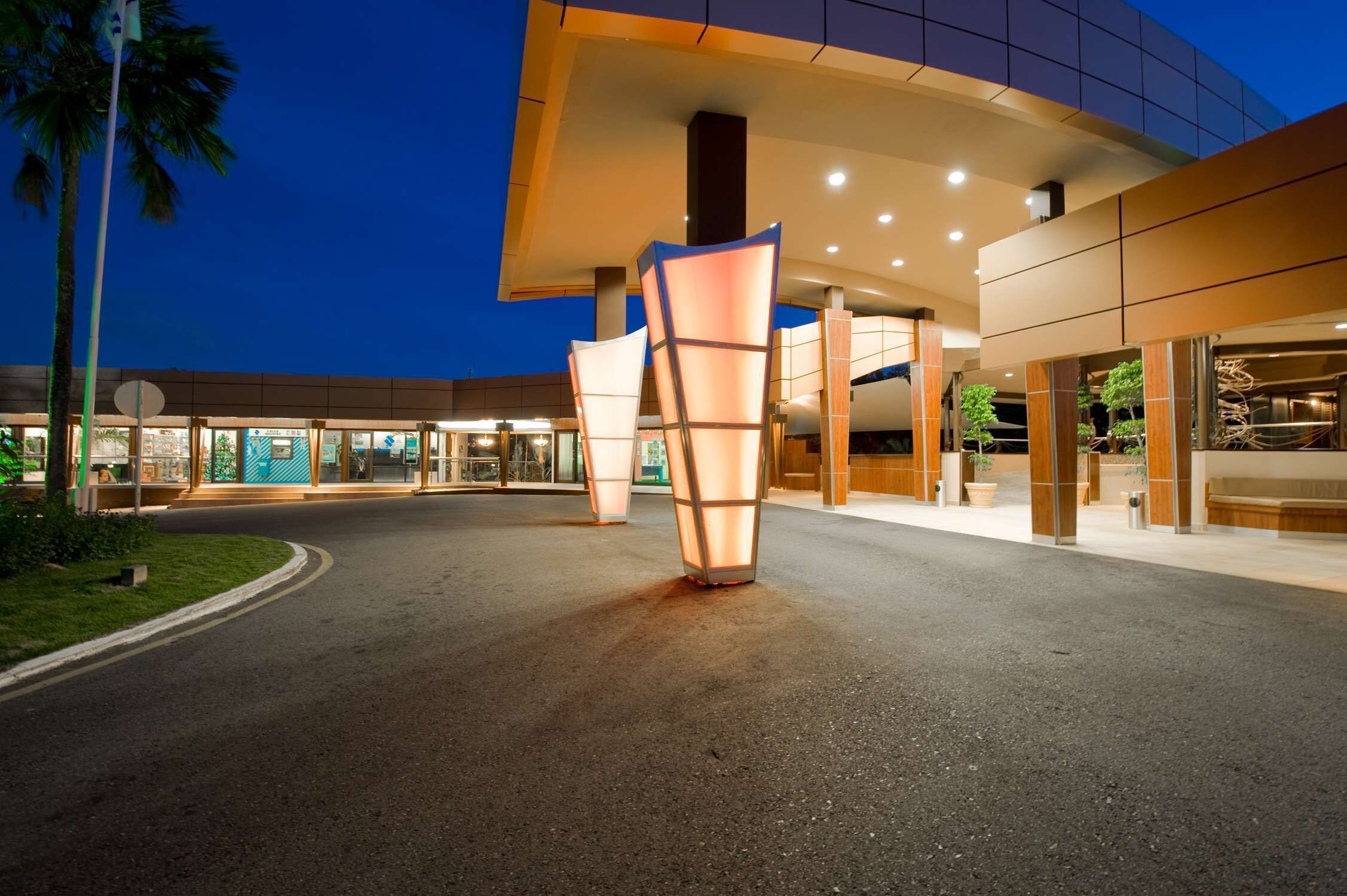Ein moderner Hotel Eingang mit gewölbtem Dach, großen Glasfenstern und einem gut beleuchteten Weg.