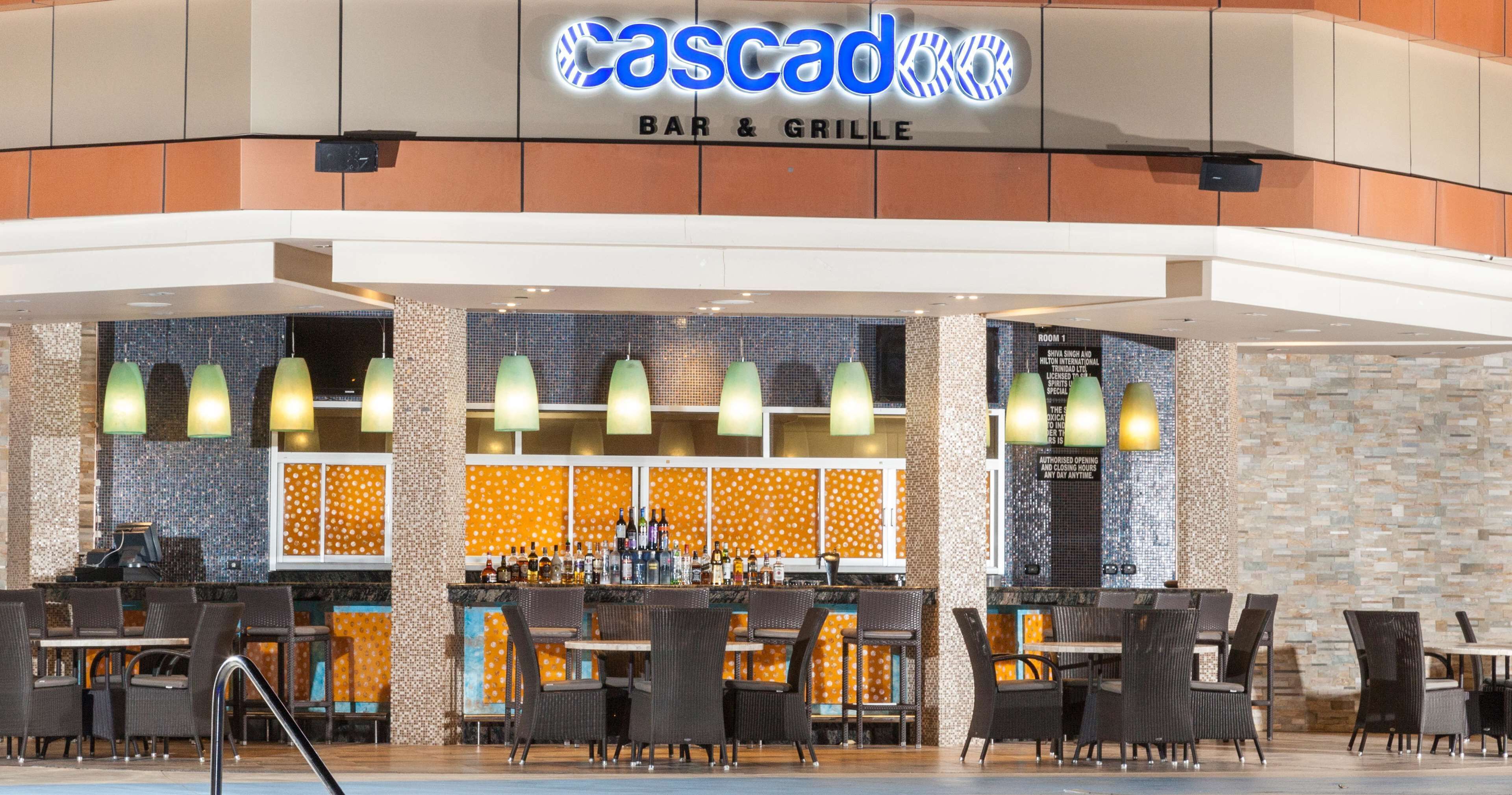 A bar and grill with a tiled backsplash, multiple hanging lights, and a variety of seating arrangements.