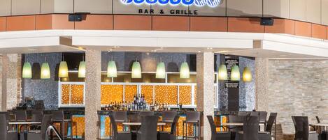 A bar and grill with a tiled backsplash, multiple hanging lights, and a variety of seating arrangements.