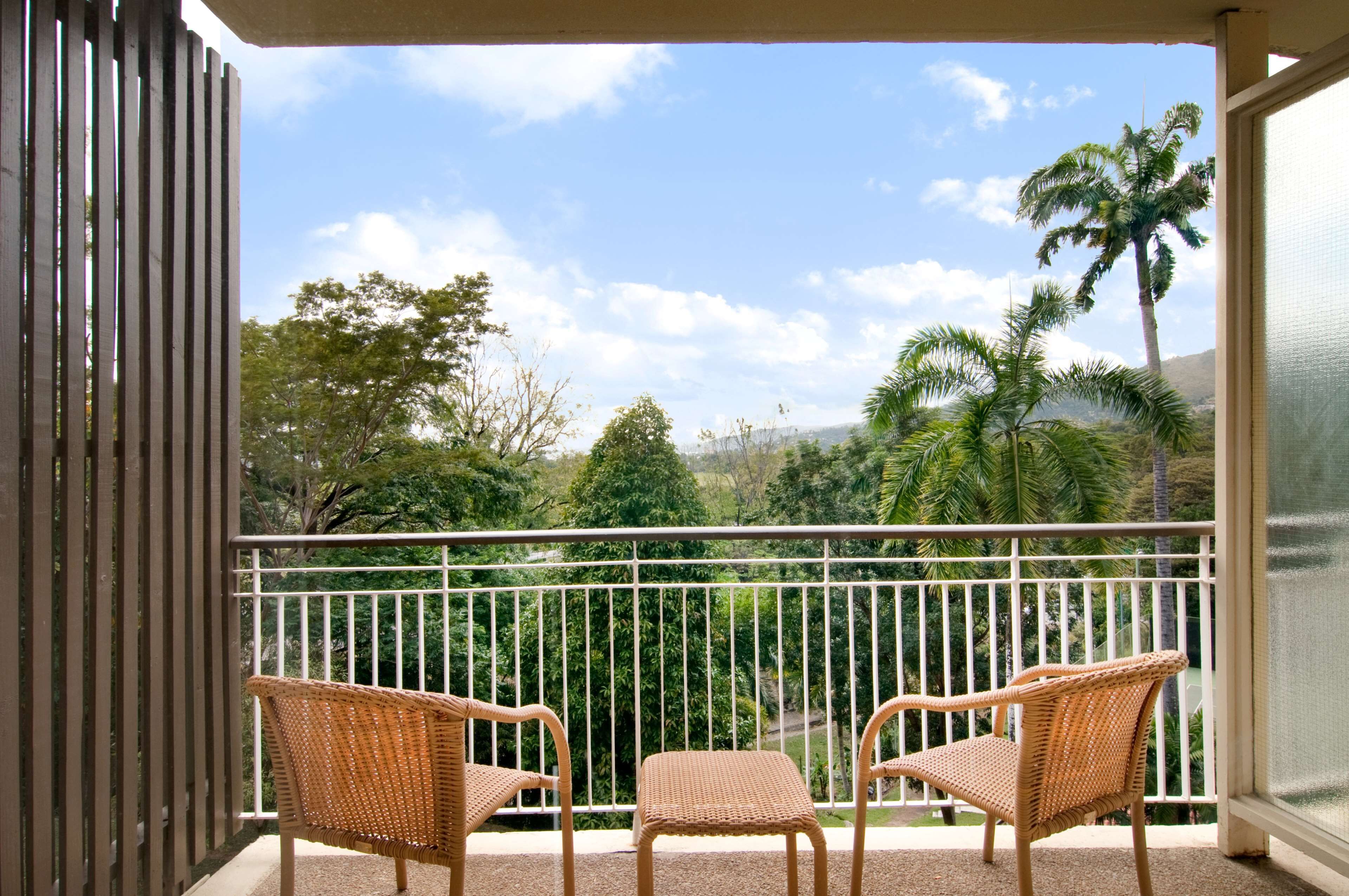 A balcony with wicker chairs and a view of tropical trees and mountains.