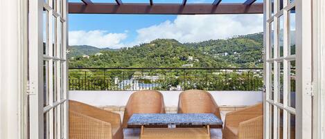 A balcony with wicker furniture and a view of a green hillside.