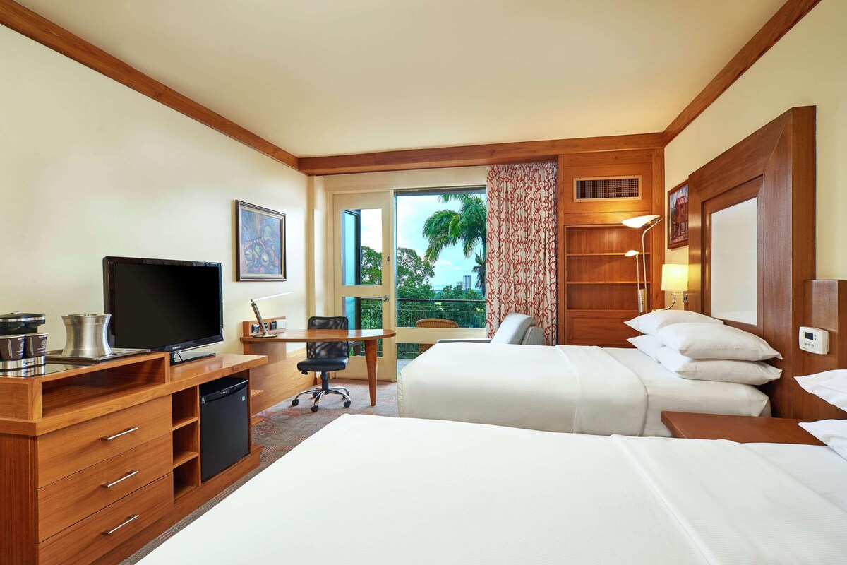 Ein Hotelzimmer mit Fernseher, Schreibtisch, Stuhl und zwei Betten.