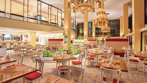A spacious hotel lobby with multiple dining areas, large windows, and a high ceiling with hanging lights. - Hilton Trinidad & Conference Centre (Port of Spain)