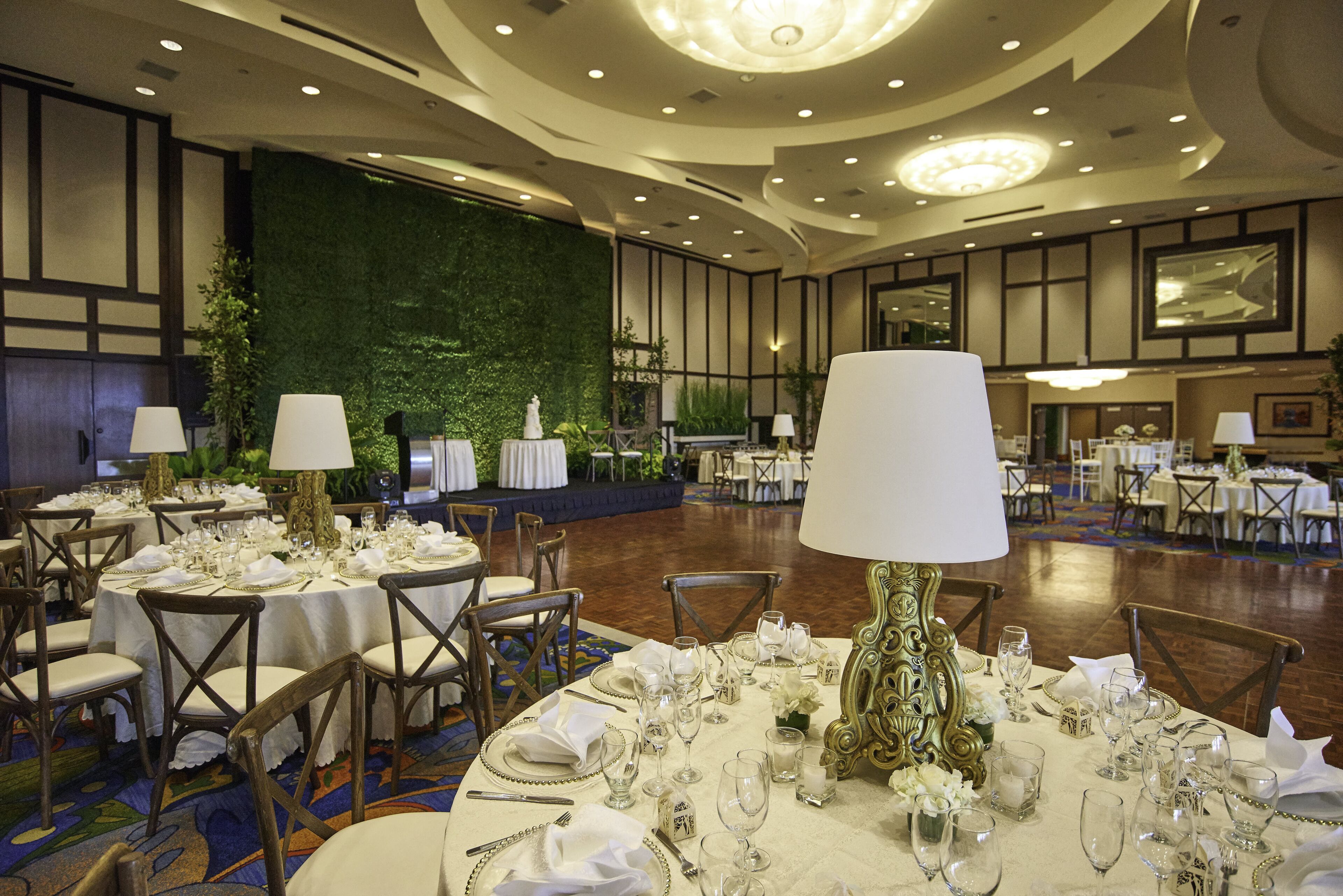 Un salón de banquetes con mesas redondas dispuestas para comer, con manteles blancos, una decoración de mesa elegante y una pared verde de fondo.
