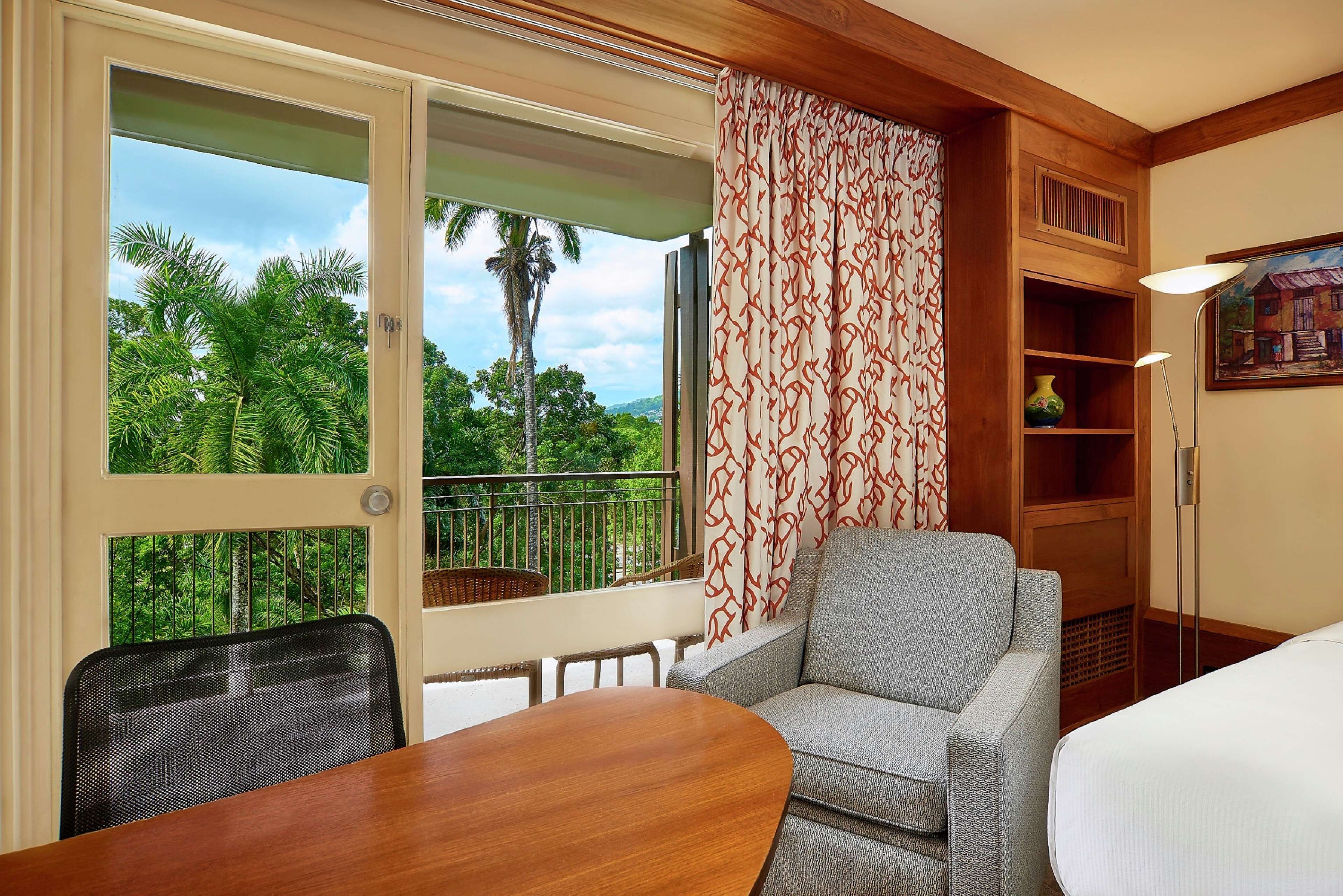 A room with a balcony, a sofa, a table, and a lamp.