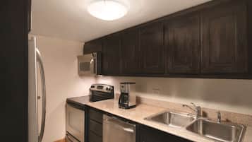 A compact kitchen with dark cabinets, stainless steel appliances, a microwave, a toaster, and a double sink.