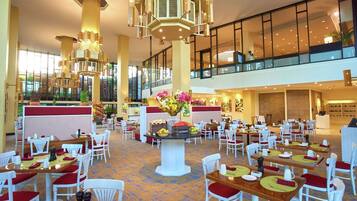 Un amplio vestíbulo de hotel con varias zonas de comedor, un arreglo floral central y un techo alto con modernas luminarias.
