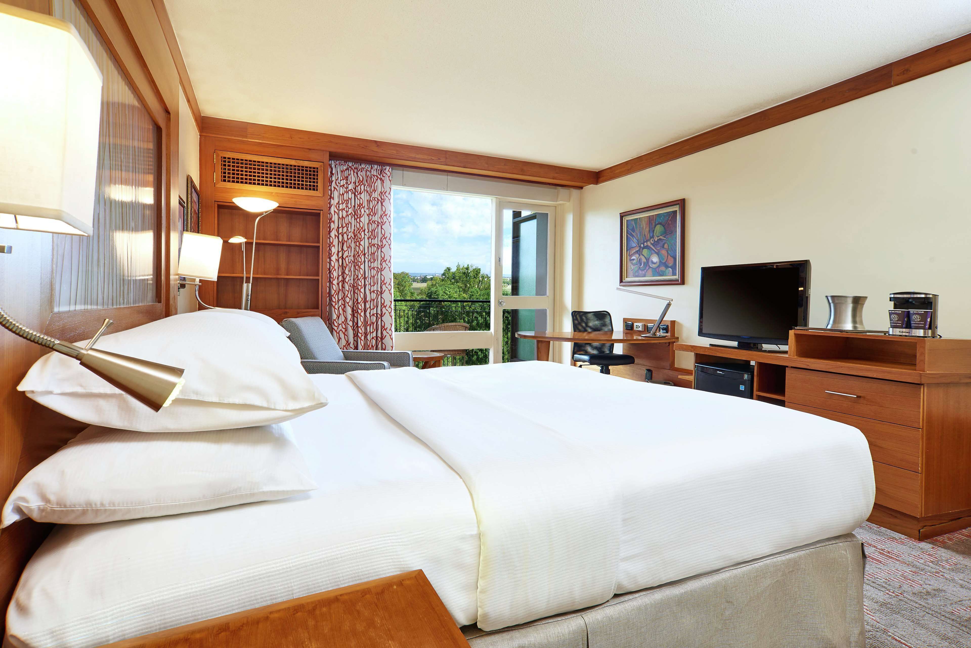 A hotel room with a bed, bedside lamps, a television, a desk, and a view of the outdoors.