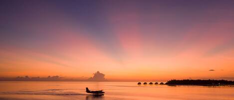 A sunset over a calm body of water with an airplane flying over it.
