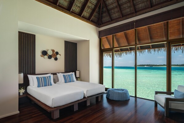 A double bed with a wooden headboard, a large window with a view of the ocean, and a thatched roof ceiling.