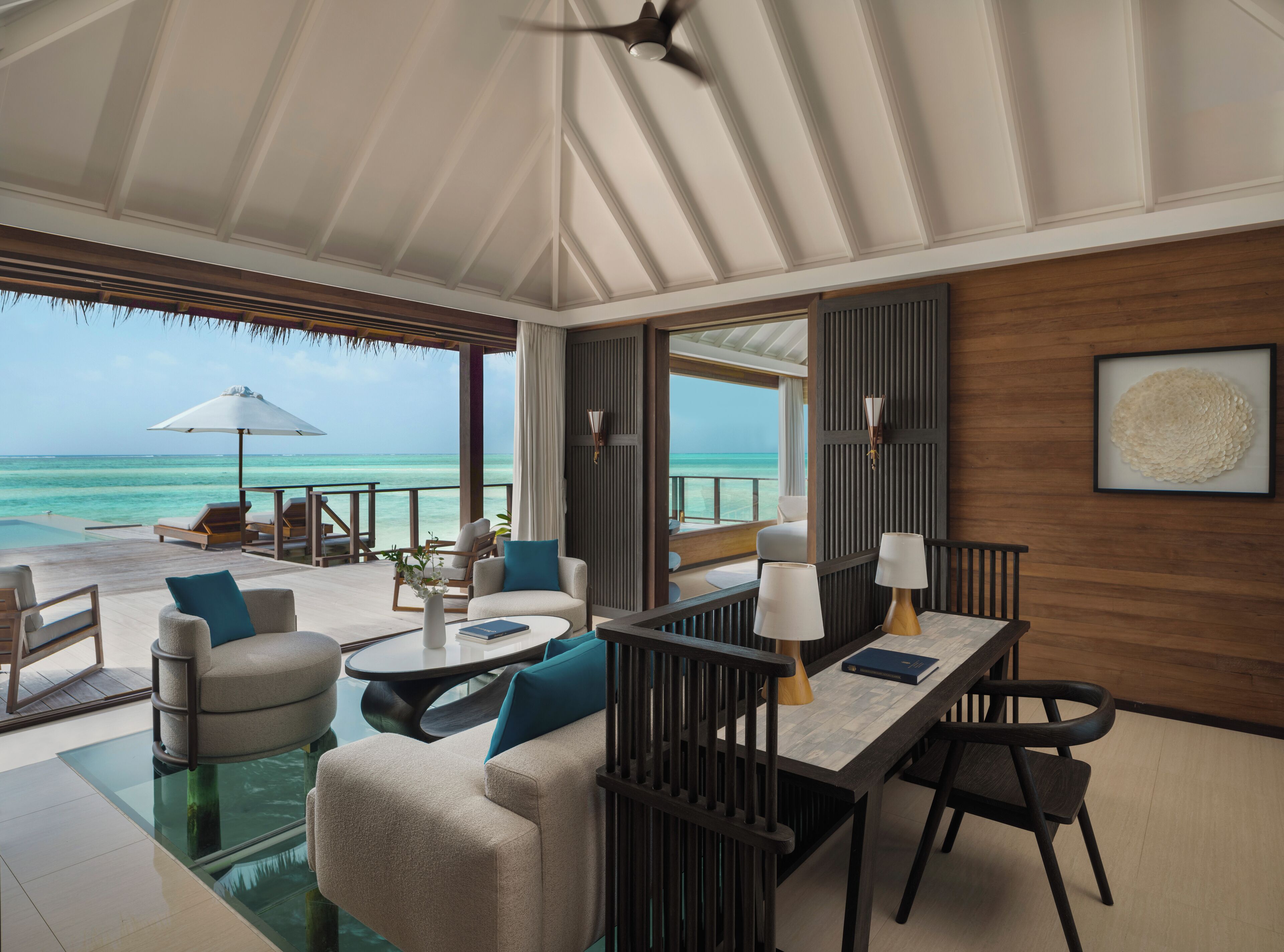 A spacious room with a large window overlooking the ocean, a seating area with a table, and a ceiling fan.