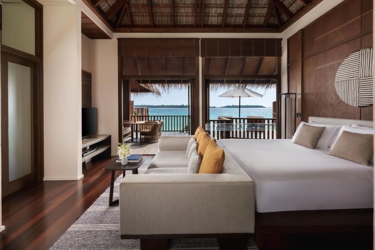 A bedroom with a large bed, a sofa, a TV, and a balcony with a view of the sea.