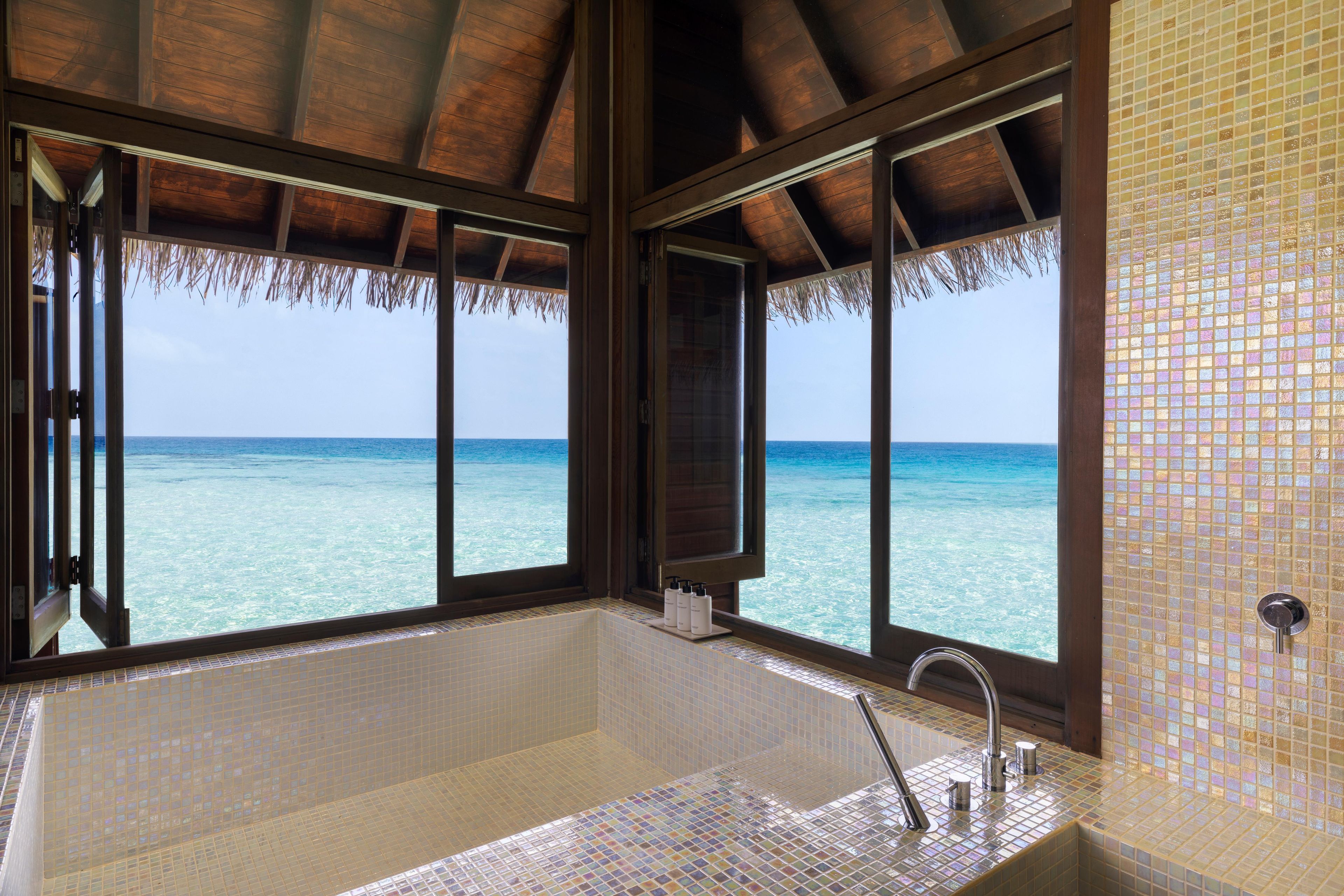 Ein Badezimmer mit einer großen Badewanne, einem Fenster mit Meerblick und einer gefliesten Wand.