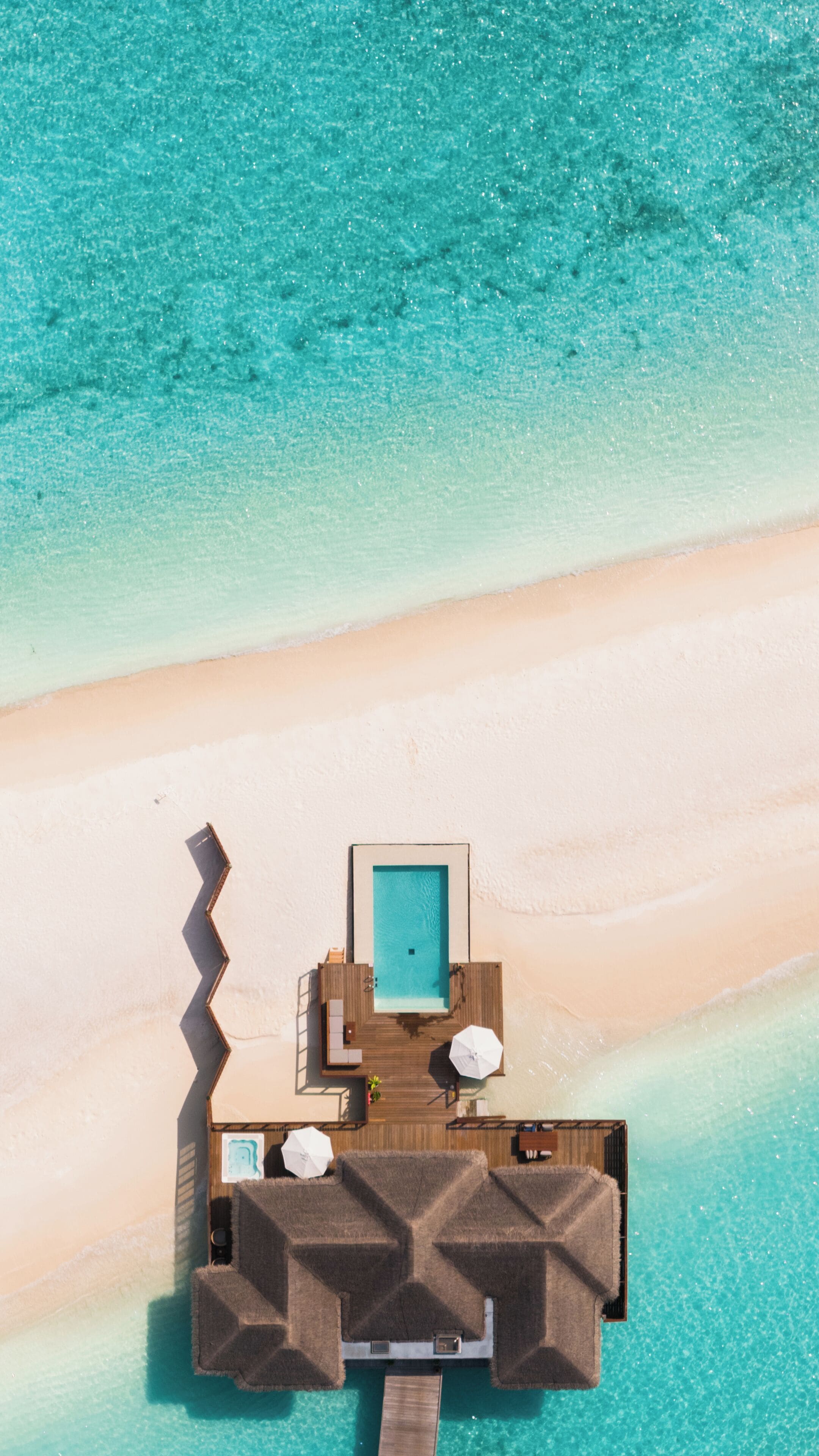 An aerial view of a beachside resort with a wooden deck, a pool, and lounge chairs.