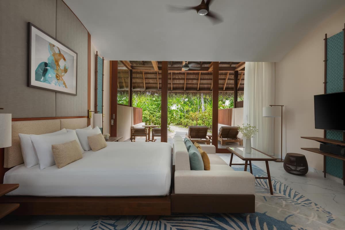 Quarto de hotel com cama, área de estar, televisão e vista para o verde.