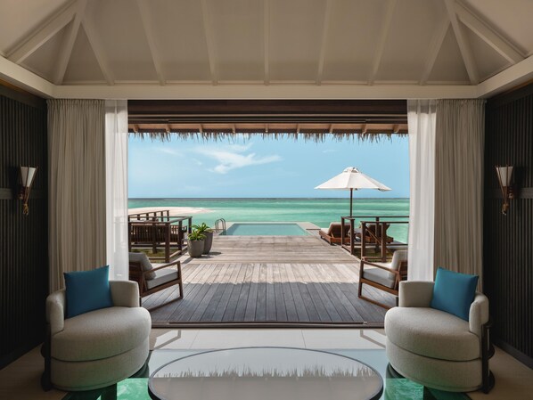 A room with a view of the ocean, a wooden deck, and a glass table.