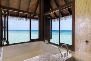 A bathroom with a large bathtub, a window with a view of the ocean, and a tiled wall. - Conrad Maldives Rangali Island (Rangalifinolhu)