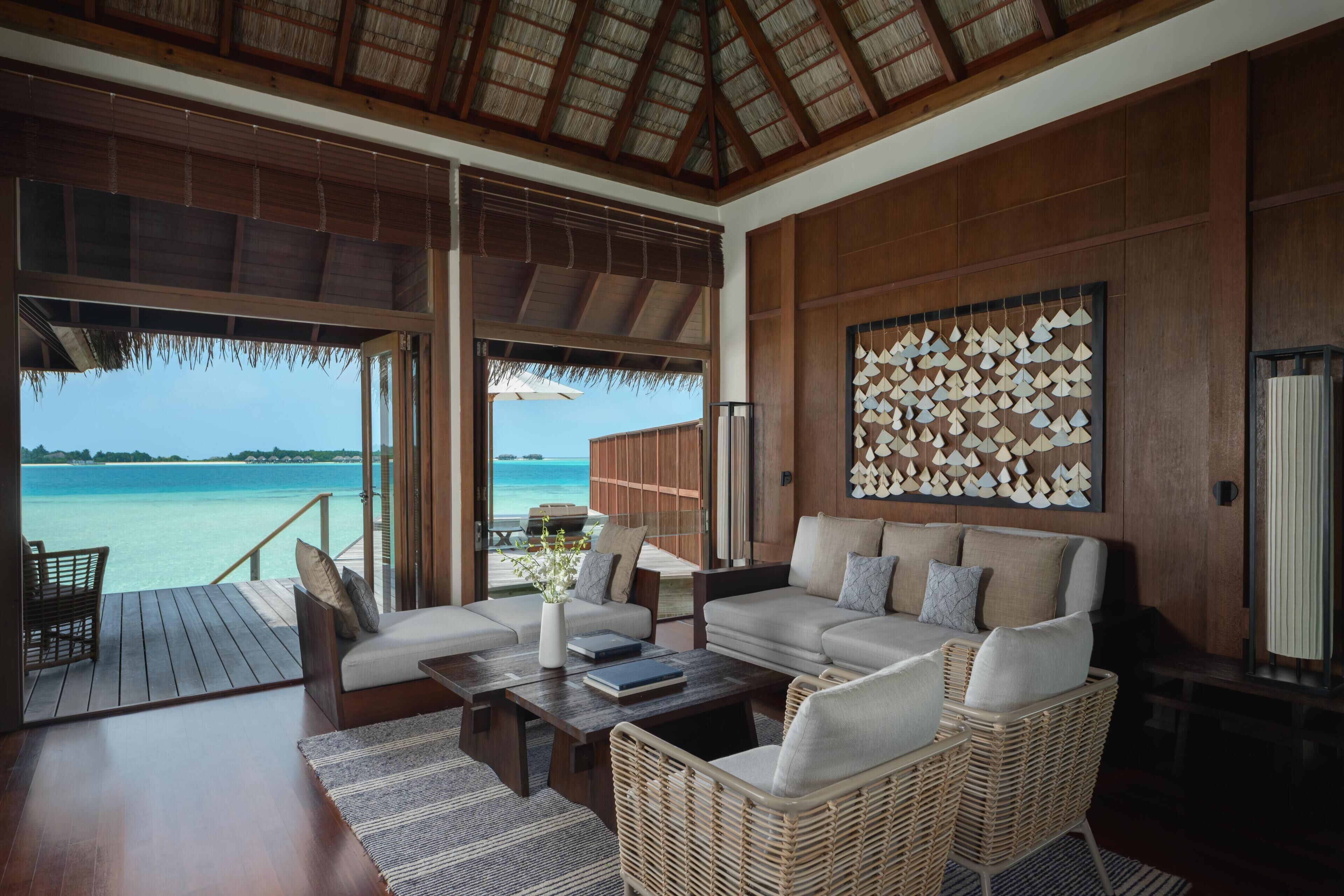 A spacious room with a large window overlooking a beach, a sofa set, a coffee table, and a wall with a geometric pattern.