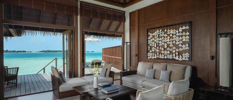A spacious room with a large window overlooking a beach, a sofa set, a coffee table, and a wall with a geometric pattern.