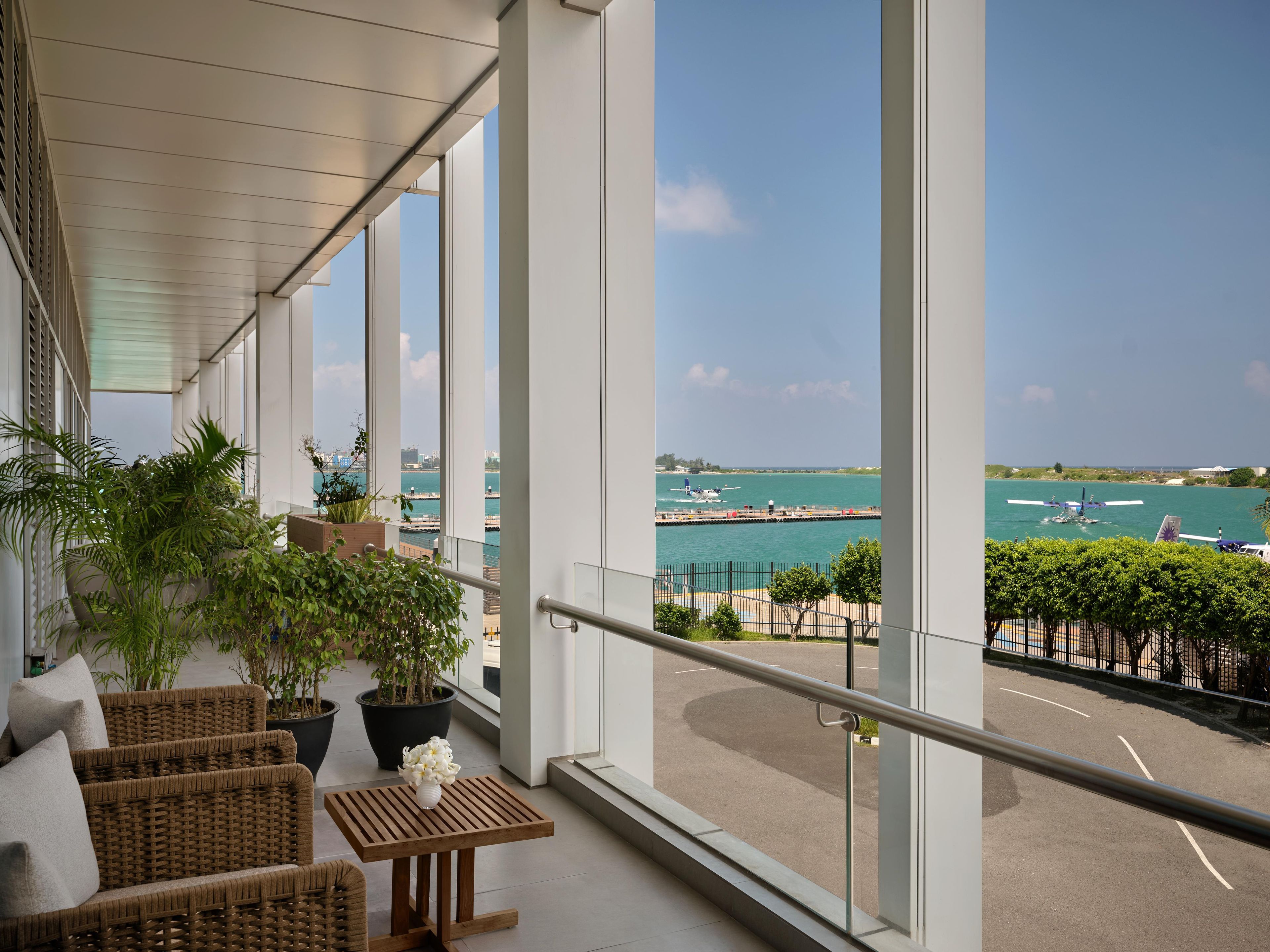 A balcony with wicker furniture, potted plants, and a view of a marina with boats.