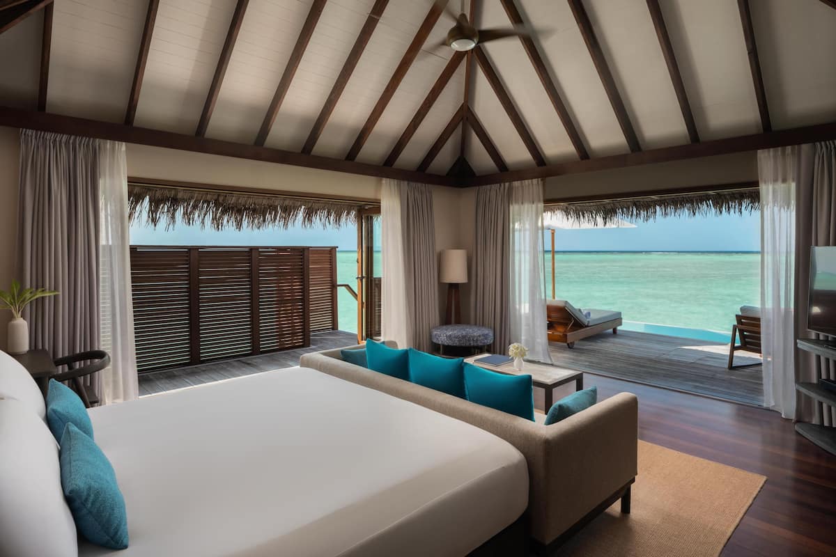 Quarto com cama grande, sofá, televisão e vista para o mar.