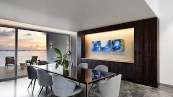 A modern dining area with a glass table, grey chairs, and a view of the sea.