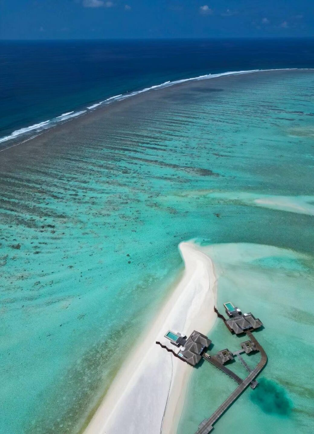 An aerial view of a beach resort with a clear pathway leading to overwater bungalows.