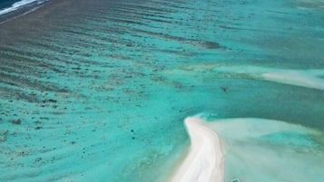 An aerial view of a beach resort with a clear pathway leading to overwater bungalows.