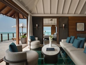 A modern suite with a glass floor, a sofa, armchairs, a coffee table, and a view of the ocean. - Conrad Maldives Rangali Island (Rangalifinolhu)
