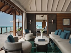 A modern suite with a glass floor, a sofa, a chair, a coffee table, and a view of the ocean.