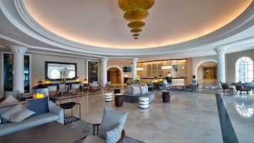 Een ruime lobby met een centrale zithoek, een receptiebalie en een grote kroonluchter.