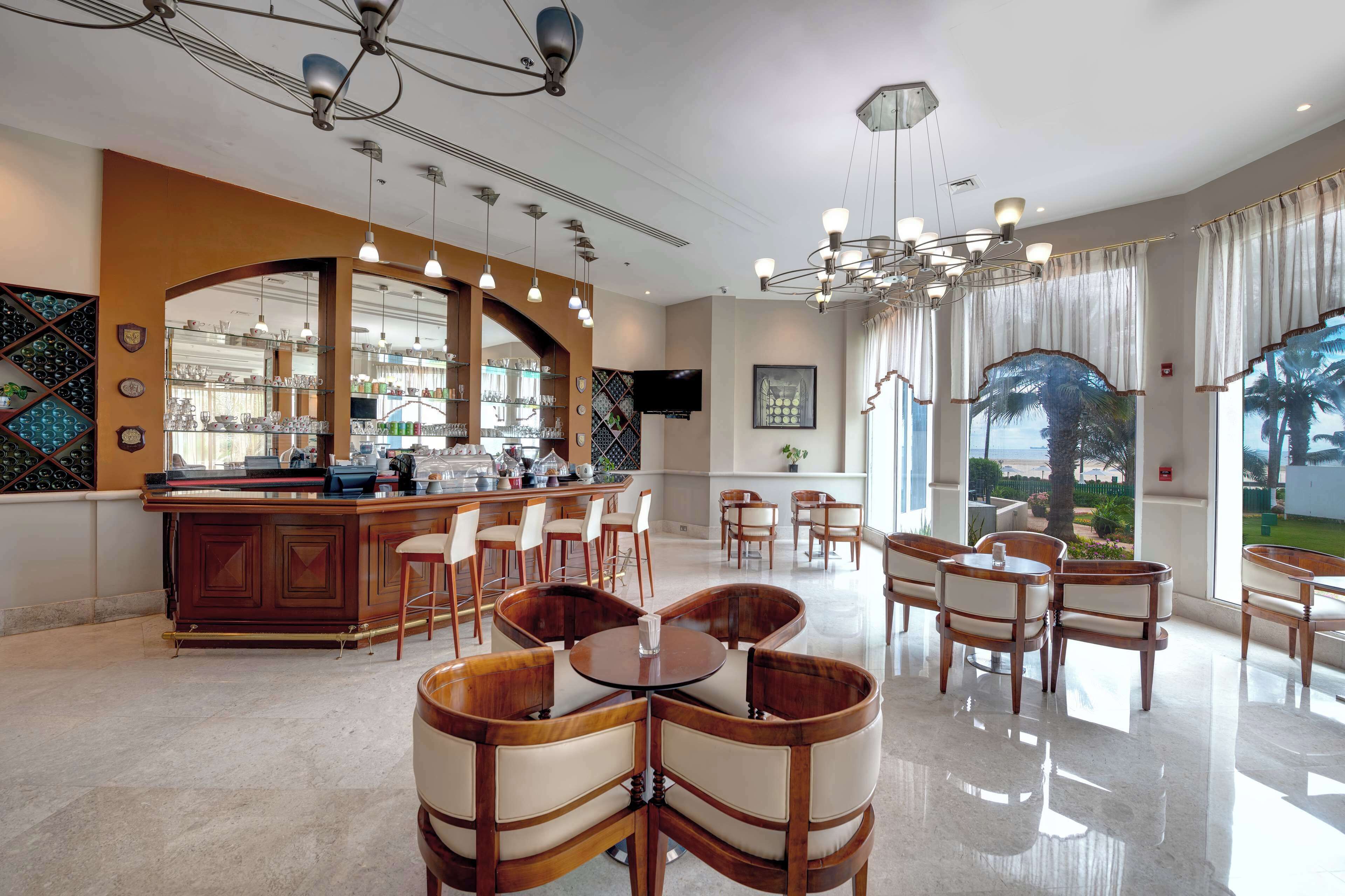 Un amplio vestíbulo de hotel con zona de bar, varios conjuntos de asientos y grandes ventanales que ofrecen vistas al exterior.