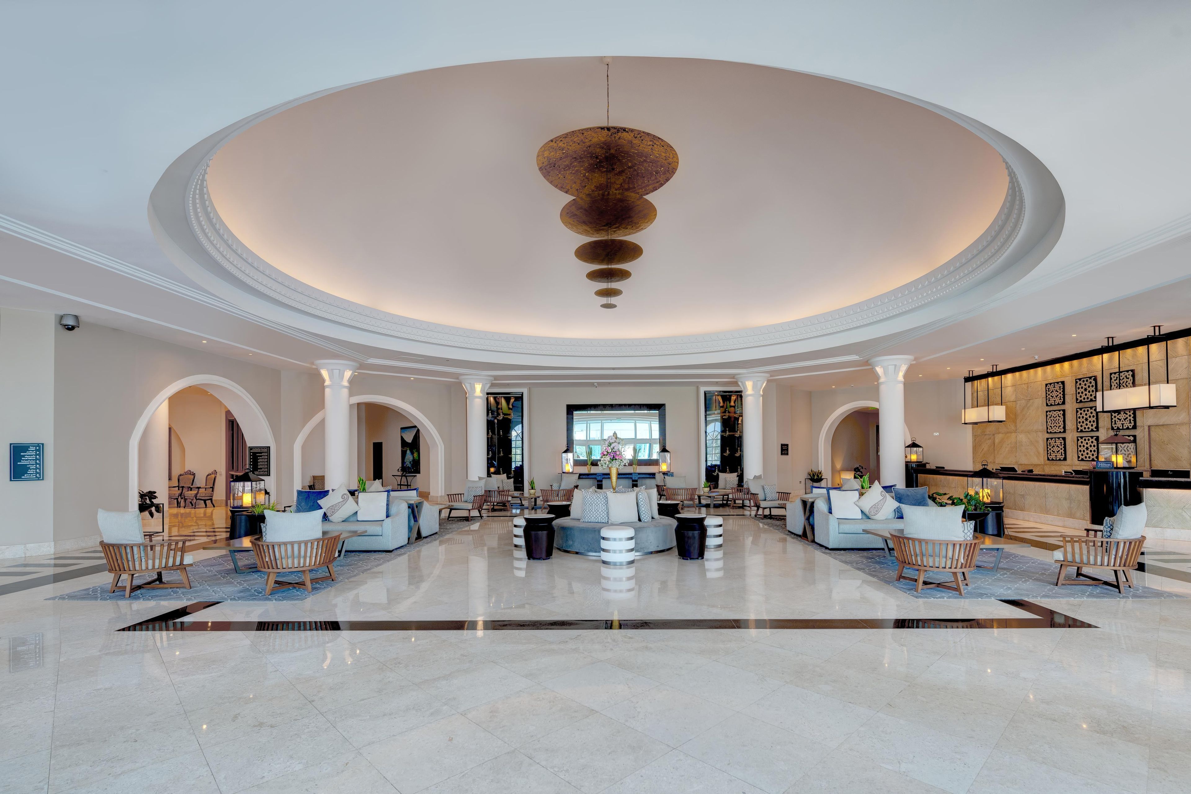 A spacious lobby with a central seating area, multiple columns, and a high ceiling with a unique light fixture.