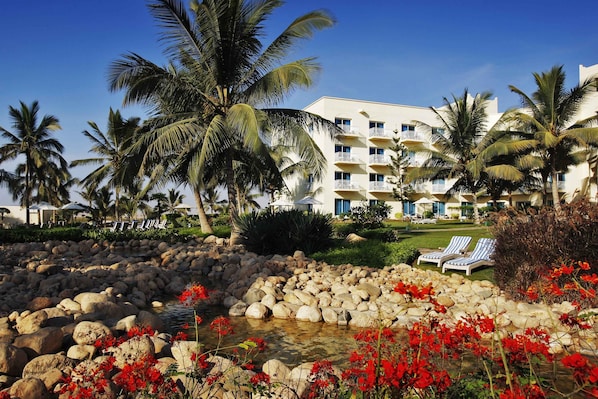 A resort with a pool surrounded by rocks and red flowers, palm trees, and a building with balconies. - Hilton Salalah Resort (Salalah)