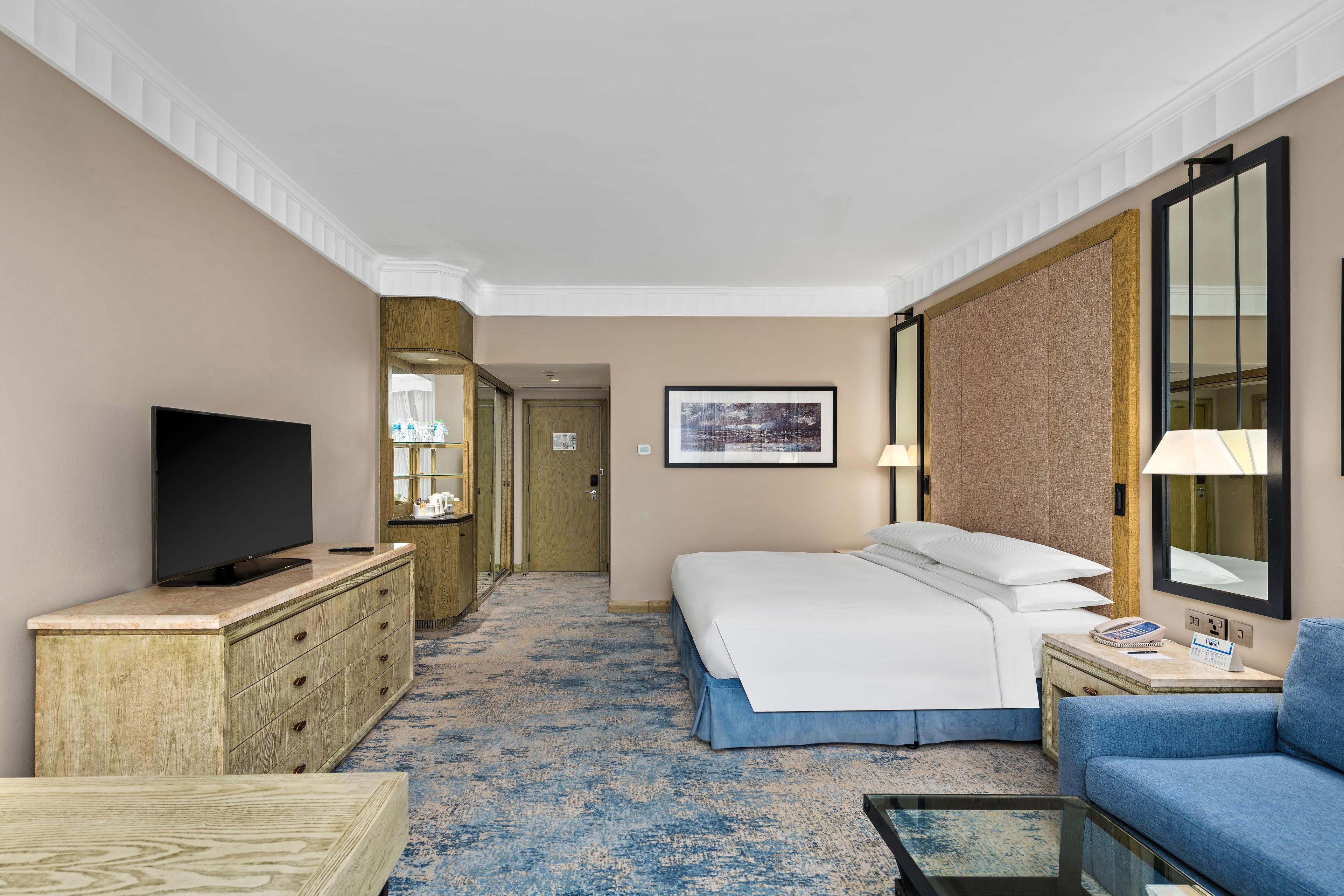 A hotel room with a bed, a television, a desk, a chair, and a large mirror.