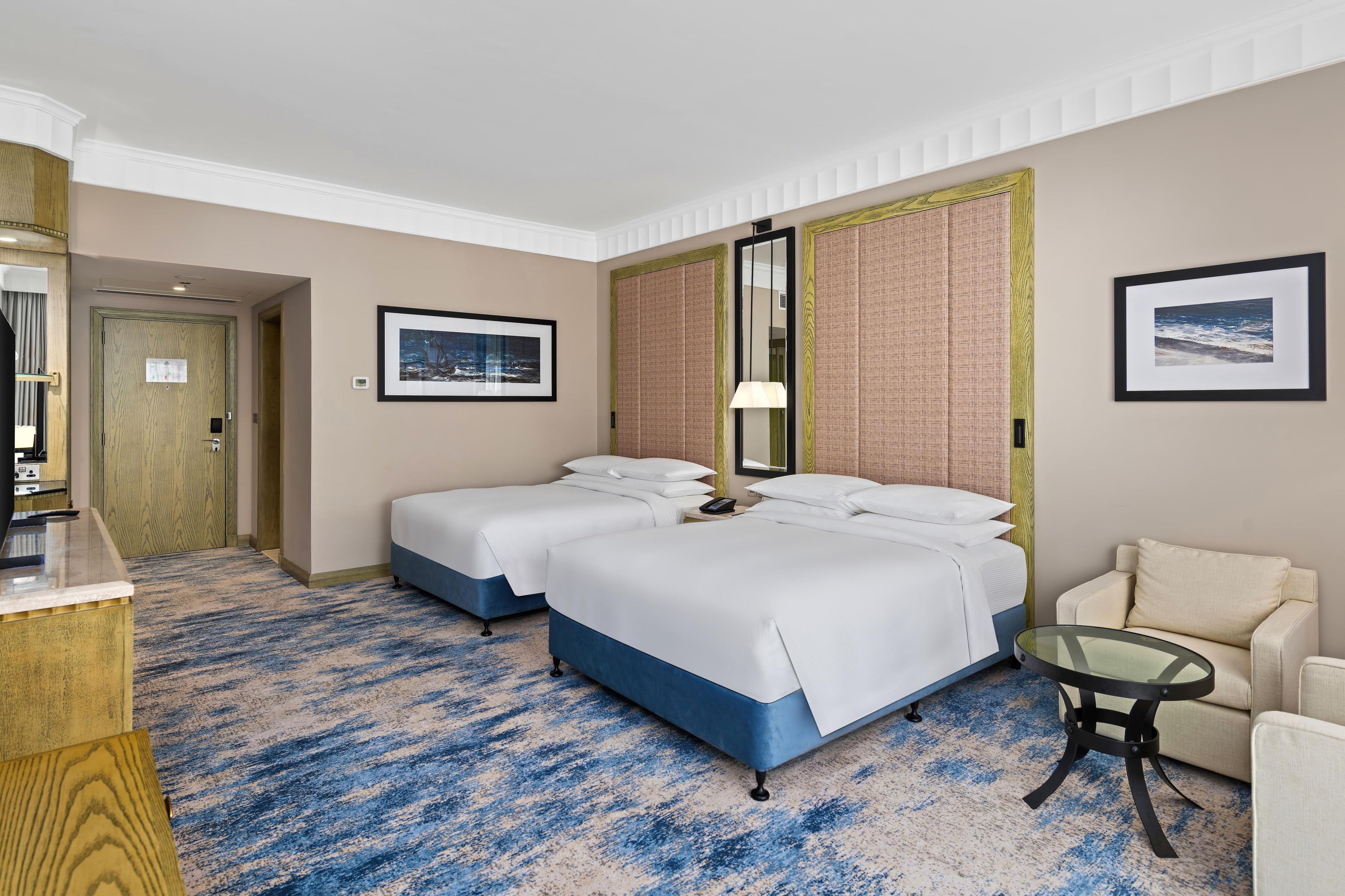 A hotel room with two beds, a desk, a chair, and a large window.