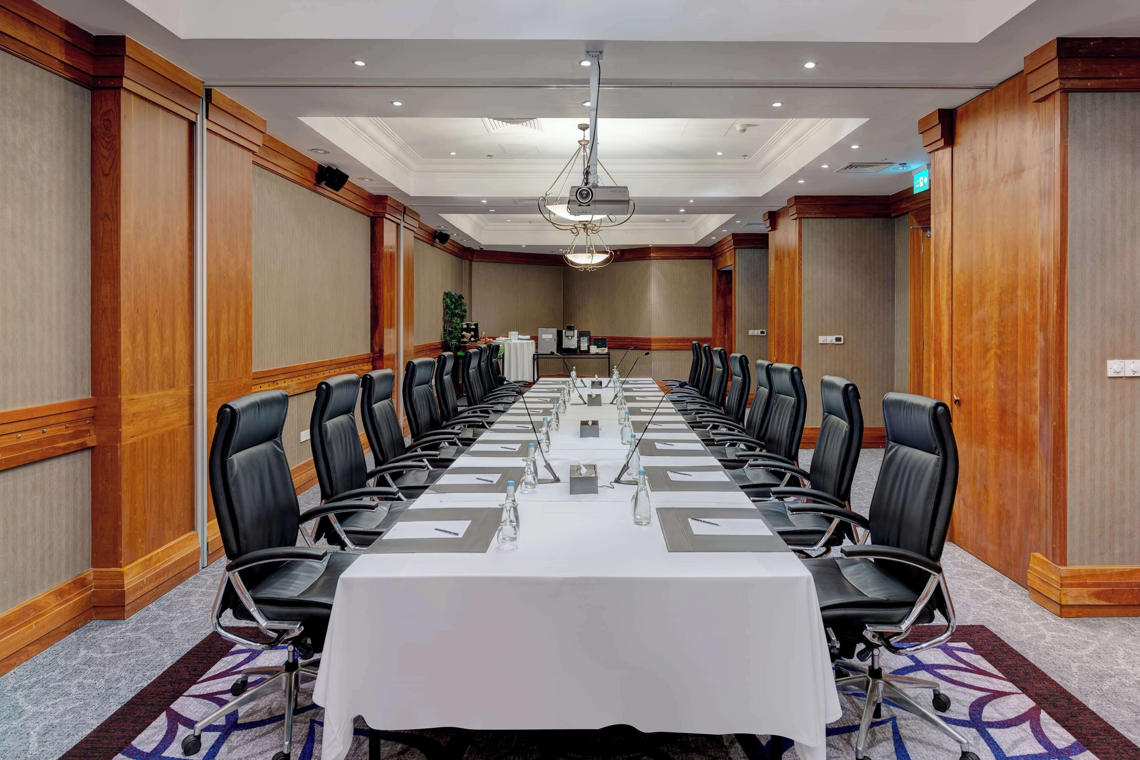 A conference room with a long table, black leather chairs, and a projector.