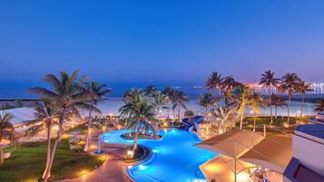 A resort pool with a curved design, surrounded by palm trees and beach views.